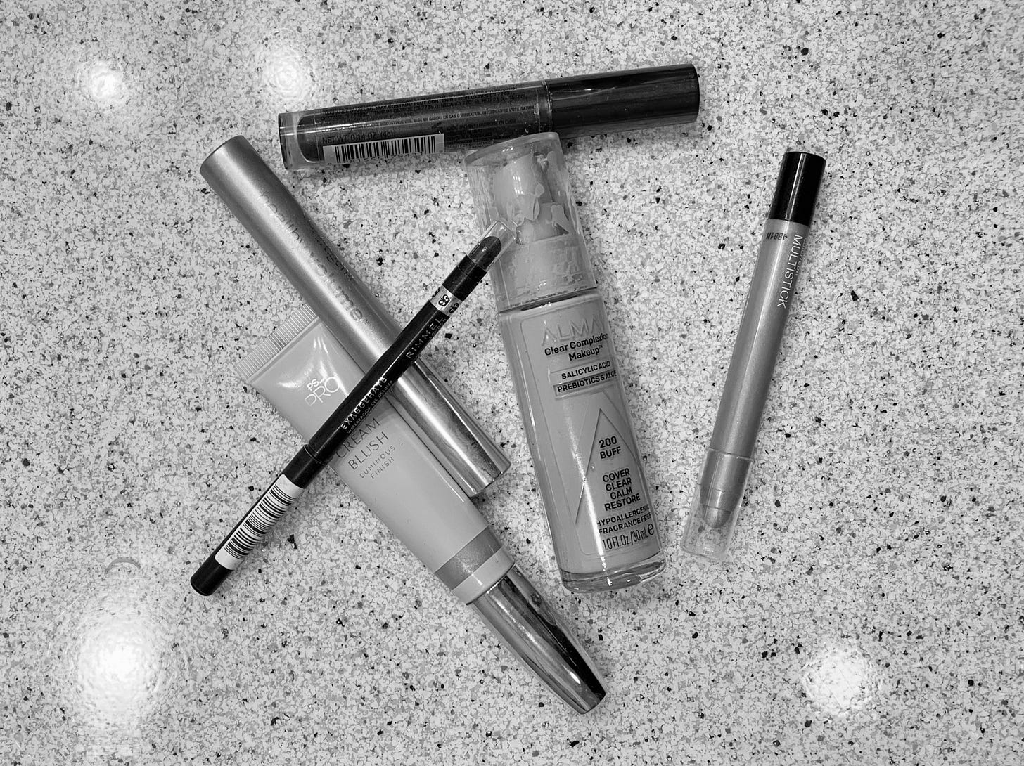 A black and white photograph of cosmetics on a bathroom counter.
