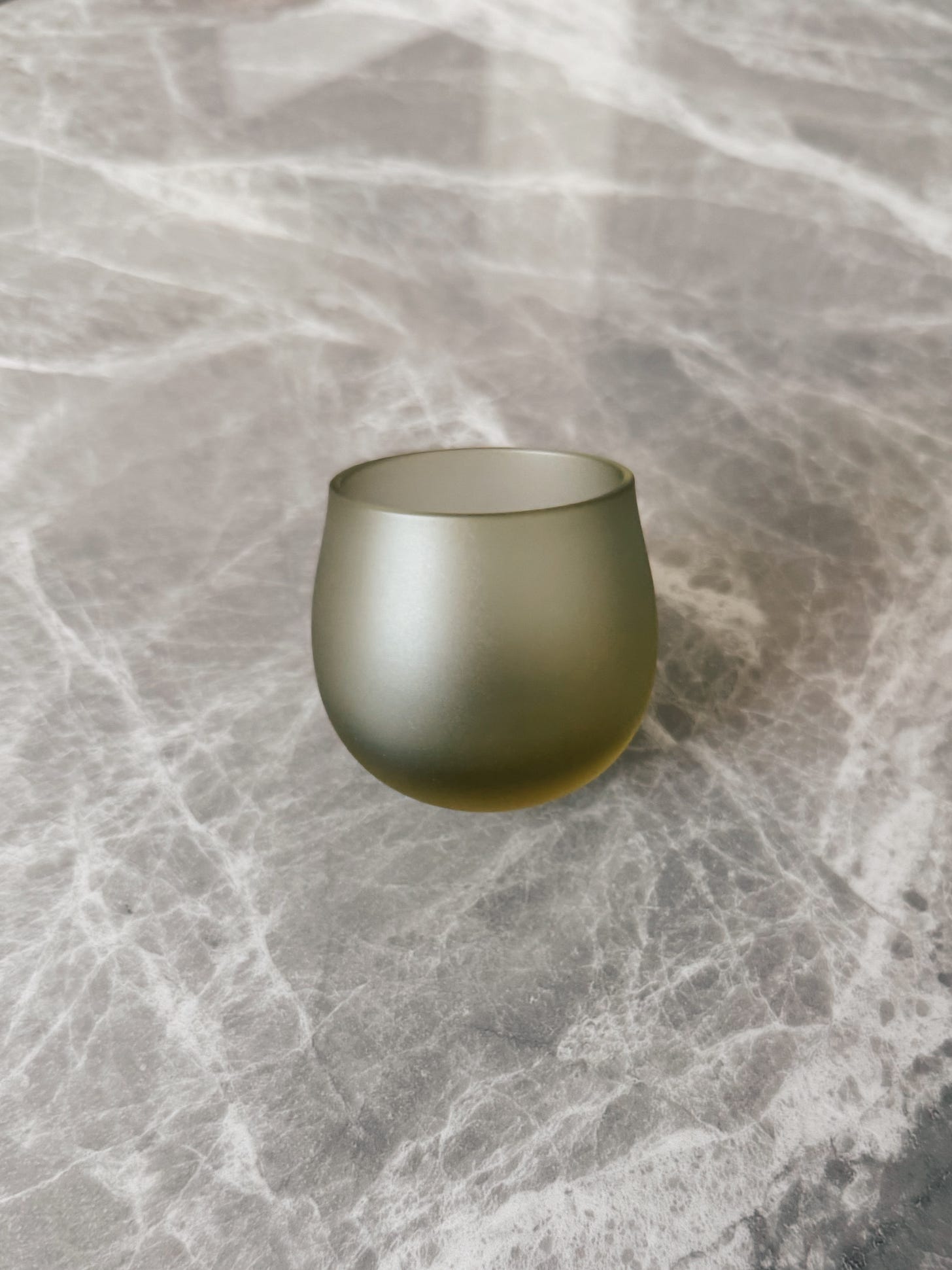 A single frosted green sake cup with a curved base in motion on a gray veined stone surface A single frosted green sake cup with a curved base in motion on a gray veined stone surface