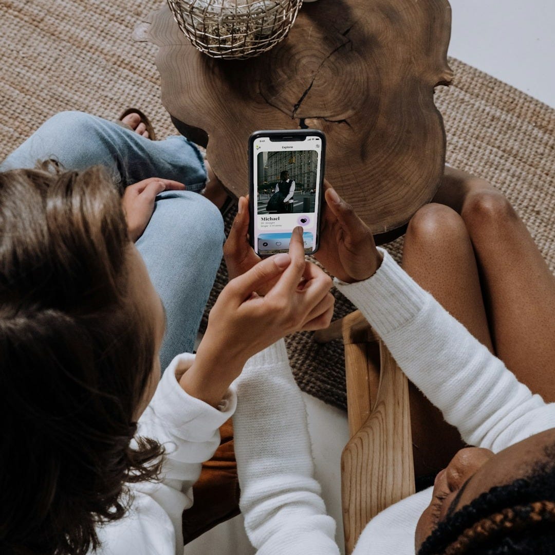 two women sitting on a couch looking at a cell phone