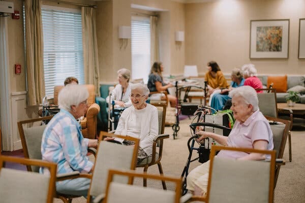 Groups of older women socialize in an institutional conference room. Groups of older women socialize in an institutional conference room.