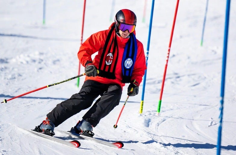 A skier in action on a snowy slope, wearing a scarf with AC Milan and Inter Milan colors, navigating a slalom course.