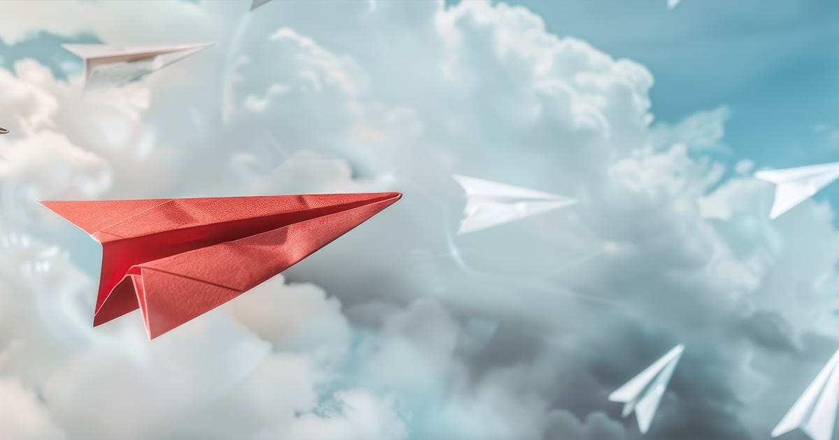 A red paper airplane flies through the clouds with a group of white paper airplanes.