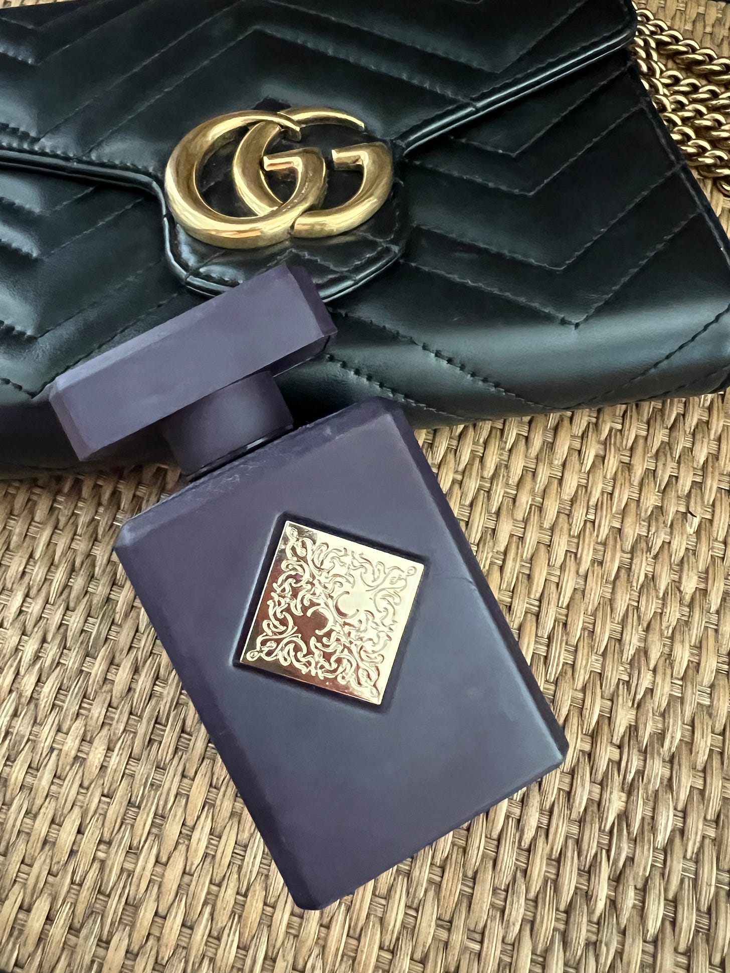 Initio Parfum Prive Side Effect fragrance bottle next to a black Gucci bag