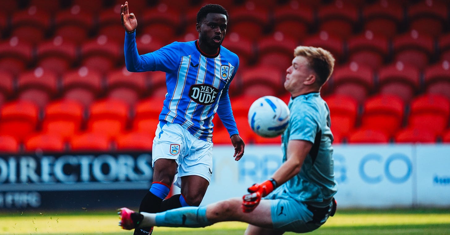 Fleetwood Town’s goalkeeper saves a shot from a Huddersfield Town player. Empty red seats can be seen in the background. Fleetwood Town’s goalkeeper saves a shot from a Huddersfield Town player. Empty red seats can be seen in the background.