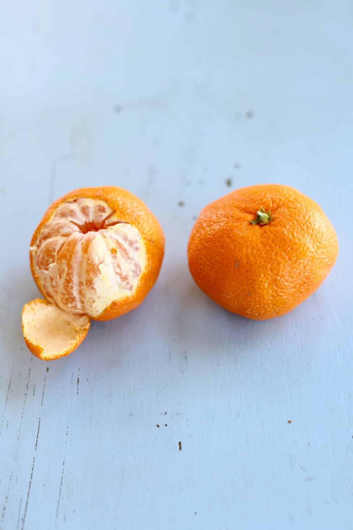 two citrus fruits, one peeled, one whole, one a blue table.