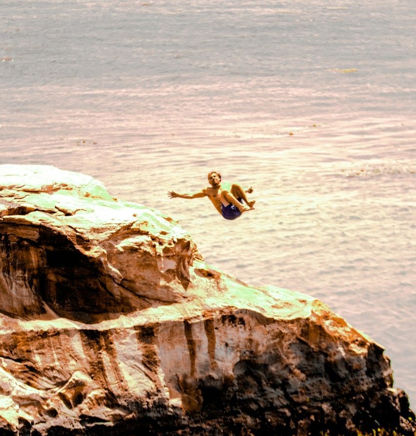 man in black shorts jumping on brown rock formation during daytime