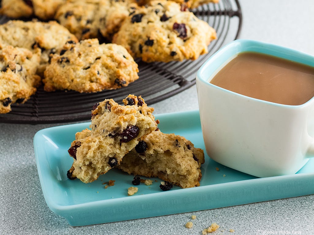 rock cakes on rack with broken rock cake and cup of tea on plate in front.