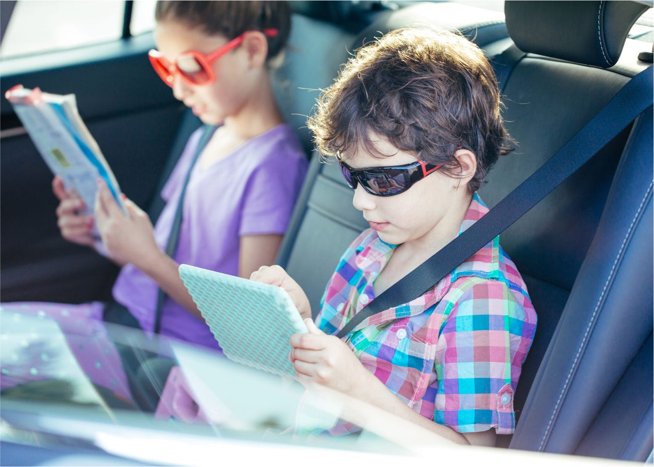 two children reading and playing in back seat of a car