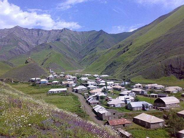 Scenic view of a small village of Siberia (Russia) surrounded by steep green mountains under a clear blue sky.