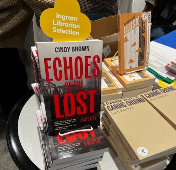 Photo 1: 2 smiling women hold copies of "Echoes of the Lost." Photo 2:  "Echoes of the Lost" on a book table, with signage that says, "Ingram Librarian Selection."