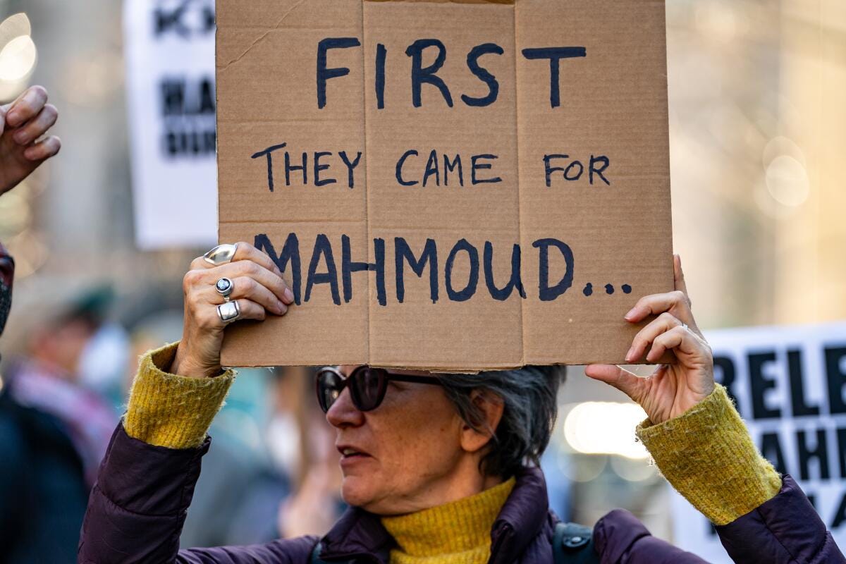 A woman with glasses holds up a cardboard sign that reads, First They Came for Mahmoud A woman with glasses holds up a cardboard sign that reads, First They Came for Mahmoud