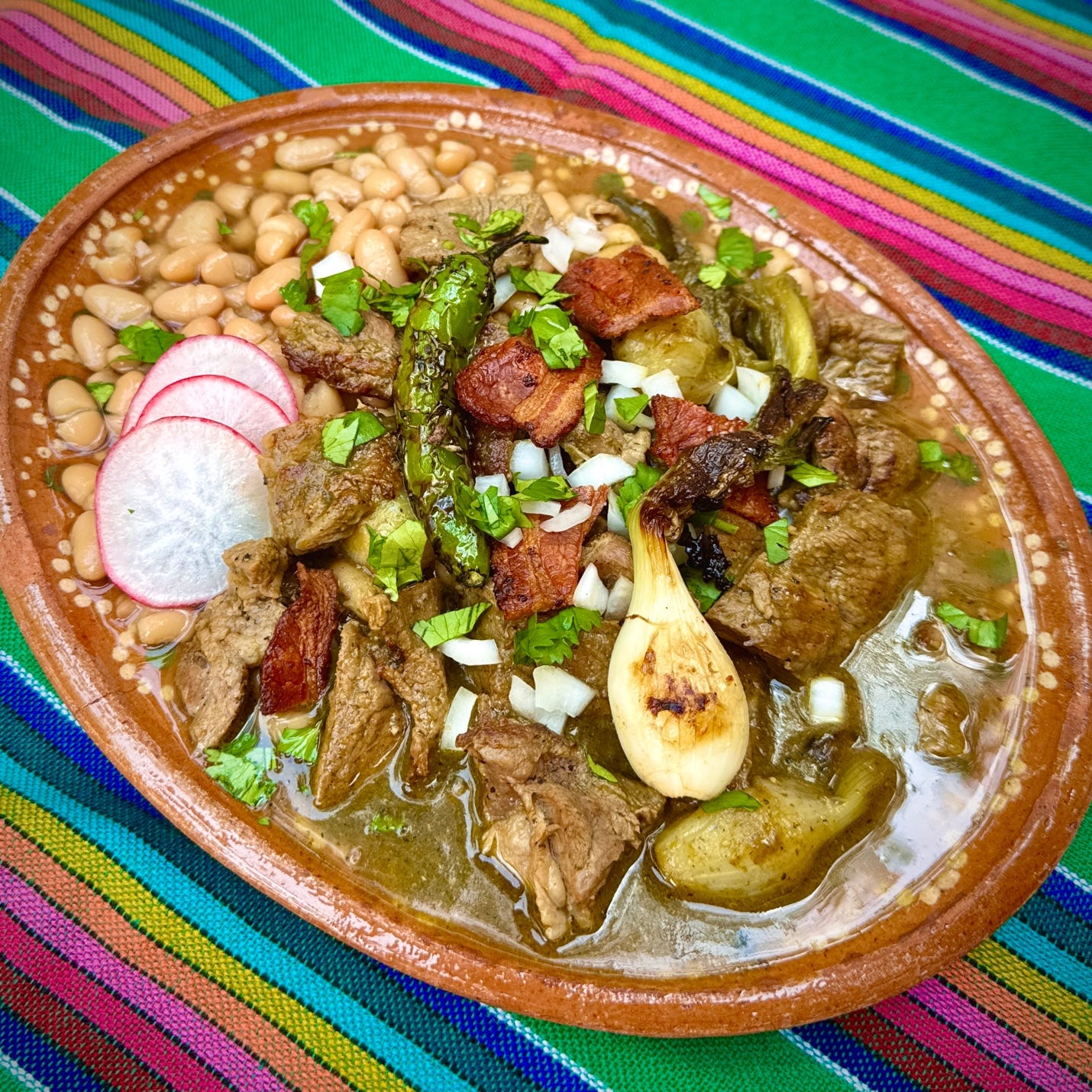 Traditional carne en su jugo served over frijoles de olla, topped with crispy bacon, cilantro, onion, and radishes, with bacon-fat-sautéed cebolla cambray and serrano.