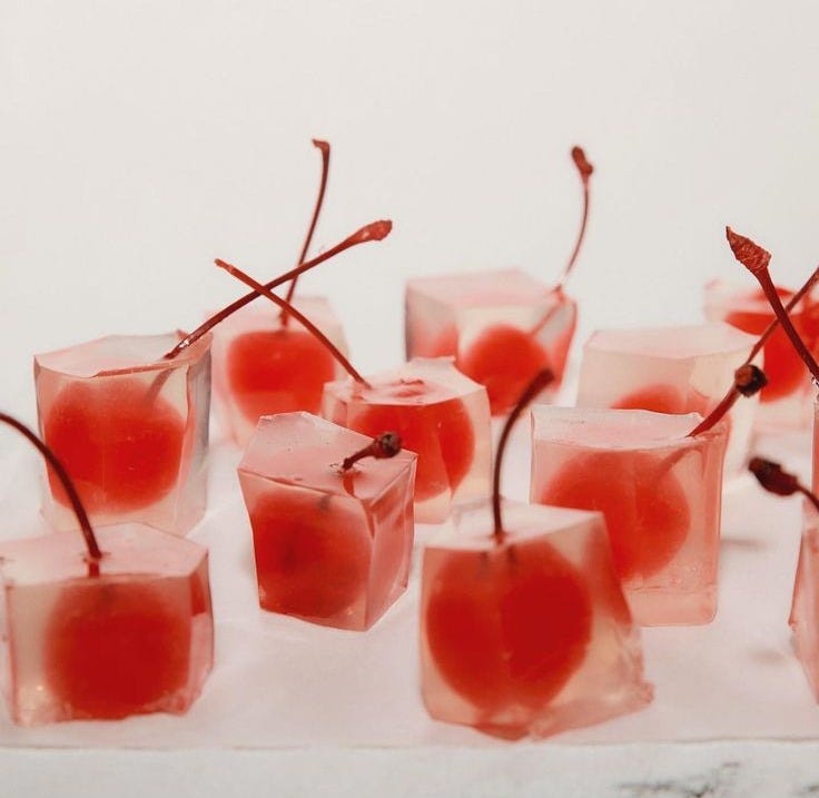 This may contain: small glasses filled with ice cubes and cherries on top of a white surface