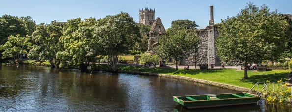 River next to castle ruins with a church in the background. 