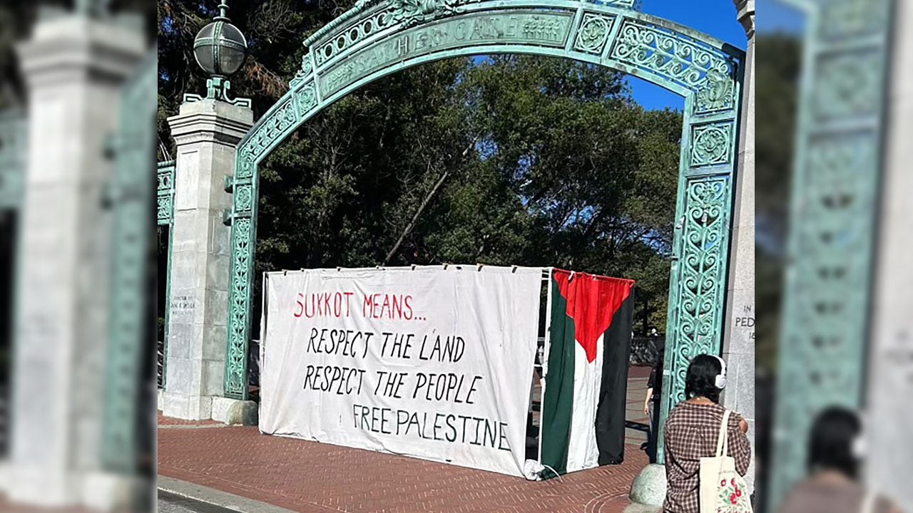 a hut with the words "Sukkot means... respect the land, respect the people, free Palestine" in the middle of a large metal gateway