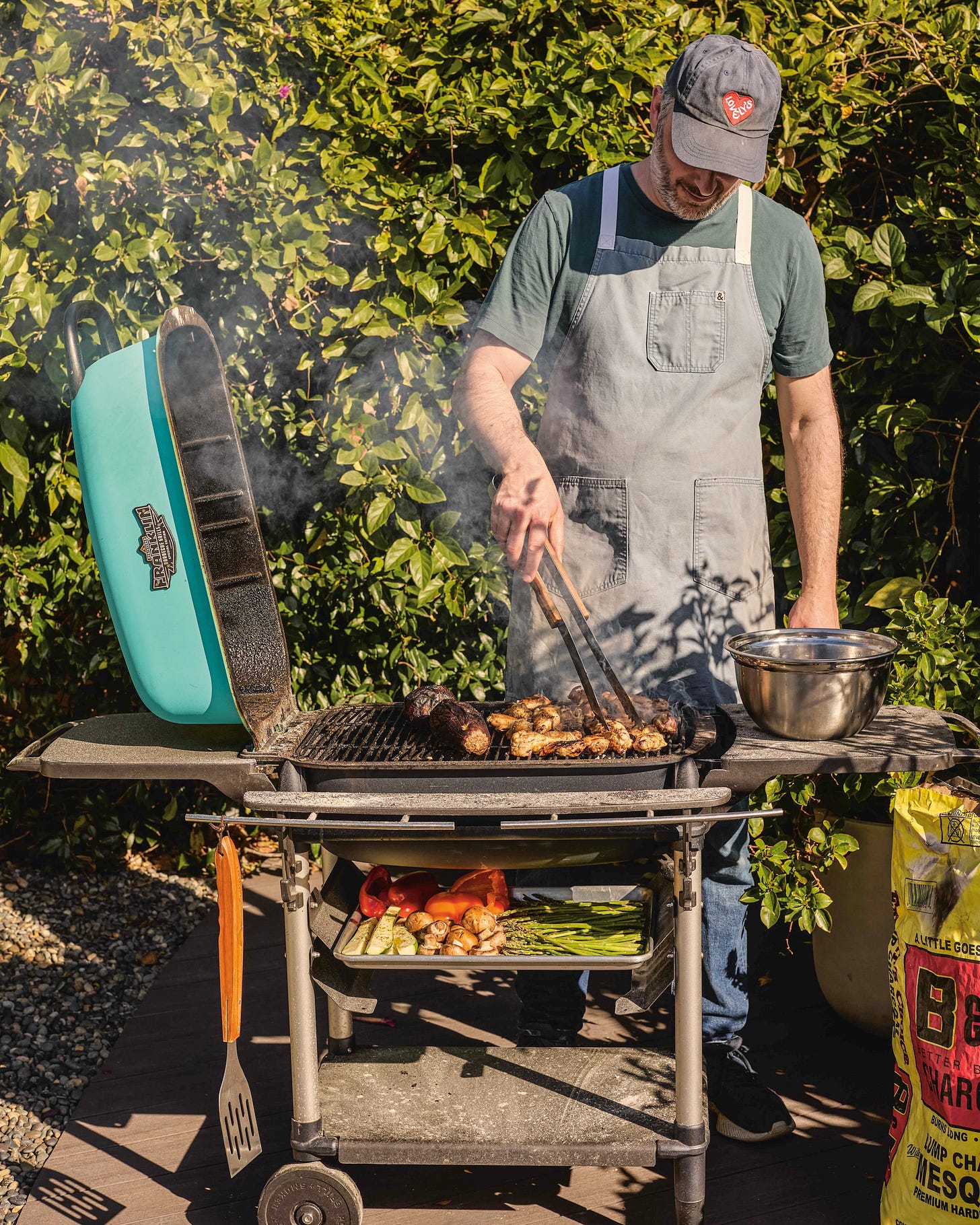 Noah Galuten outside grill meat and veggies and wearing his chef apron (Photo Credit: Kristin Teig)