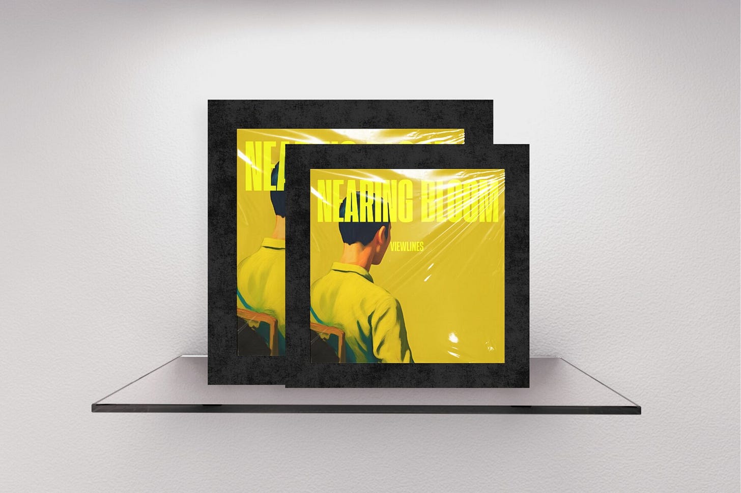 Two staggered magazine covers with thick textured black borders on a gallery shelf. The front cover features a vibrant yellow backdrop with a man seen from behind, sitting in a wooden chair and looking away into the empty space. Bold typography reading "NEARING BLOOM" overlays the image. Part of the Viewlines series at The Subtext Review.