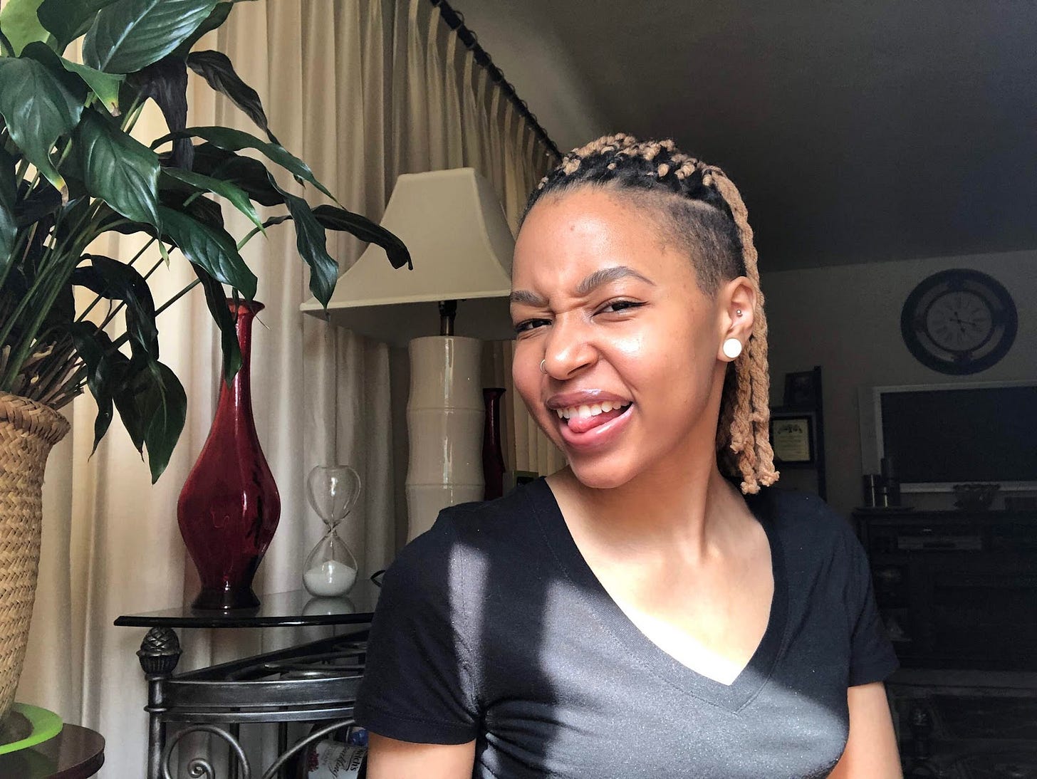 Black girl scrunching up her face and sticking tongue out with black shirt, saved sides and blond yarn braids on top of her head