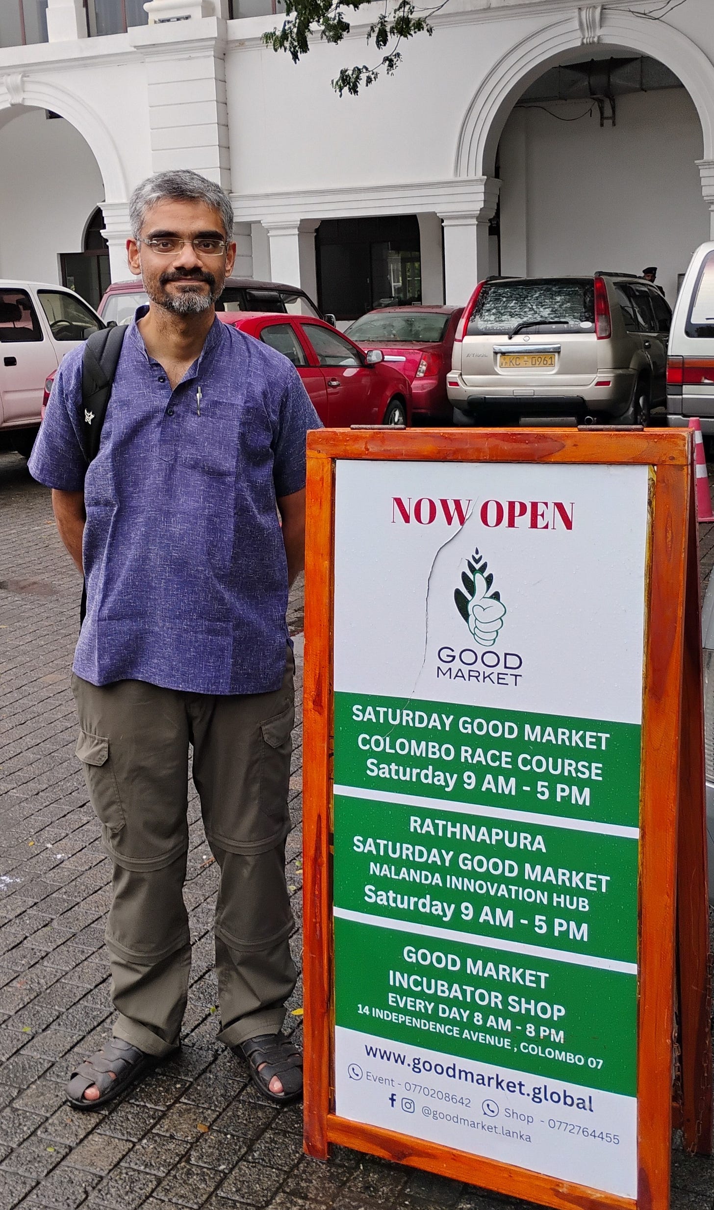 Man standing next to sign reading Saturday Good Market in Colombo, Sri Lanka