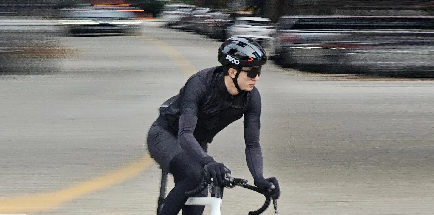 Cyclist riding down a city street with blurred background wearing a Black PIKIO helmet. Cyclist riding down a city street with blurred background wearing a Black PIKIO helmet.