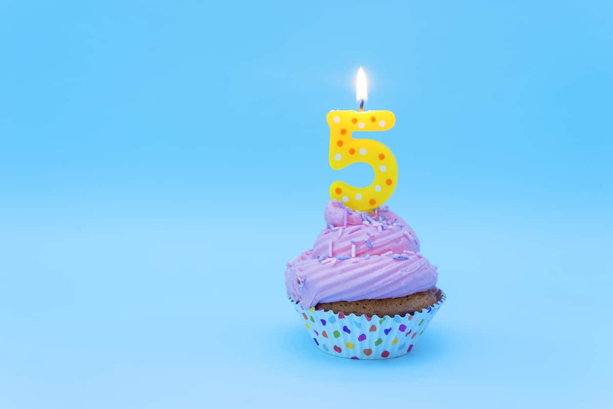 Cupcake with pink icing and a birthday candle lit in the shape of the number 5
