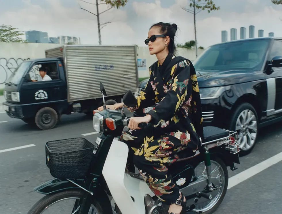 Model wearing Lemaire driving on a bike through Vietnam traffic