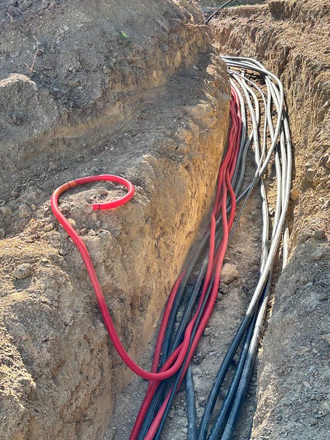 Pool construction at the château, with a concrete truck pouring beside the towers, a pool shell with pipes, and a trench of electrical cable;