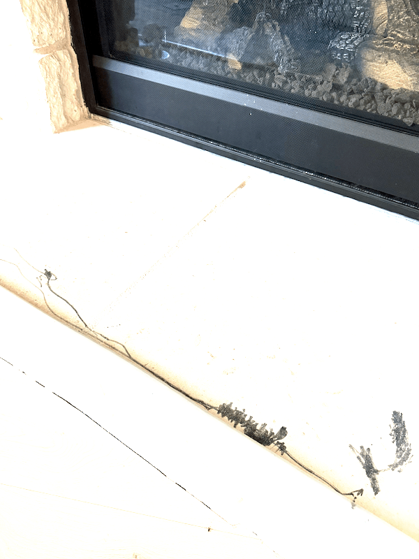 A close-up view of a fireplace mantel showing marks and smudges, possibly from a child using a black marker on the surface.