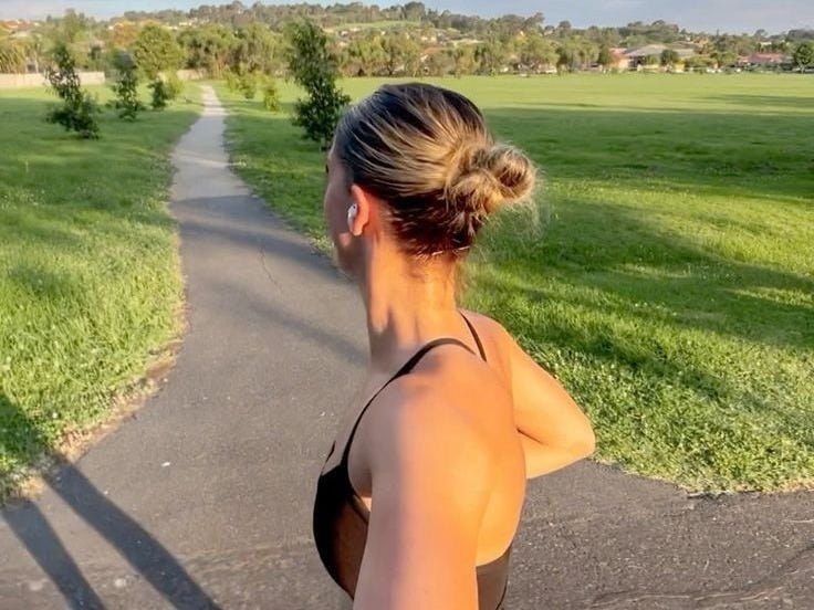 This may contain: a woman is running down the road with her shadow on the ground and grass in the background