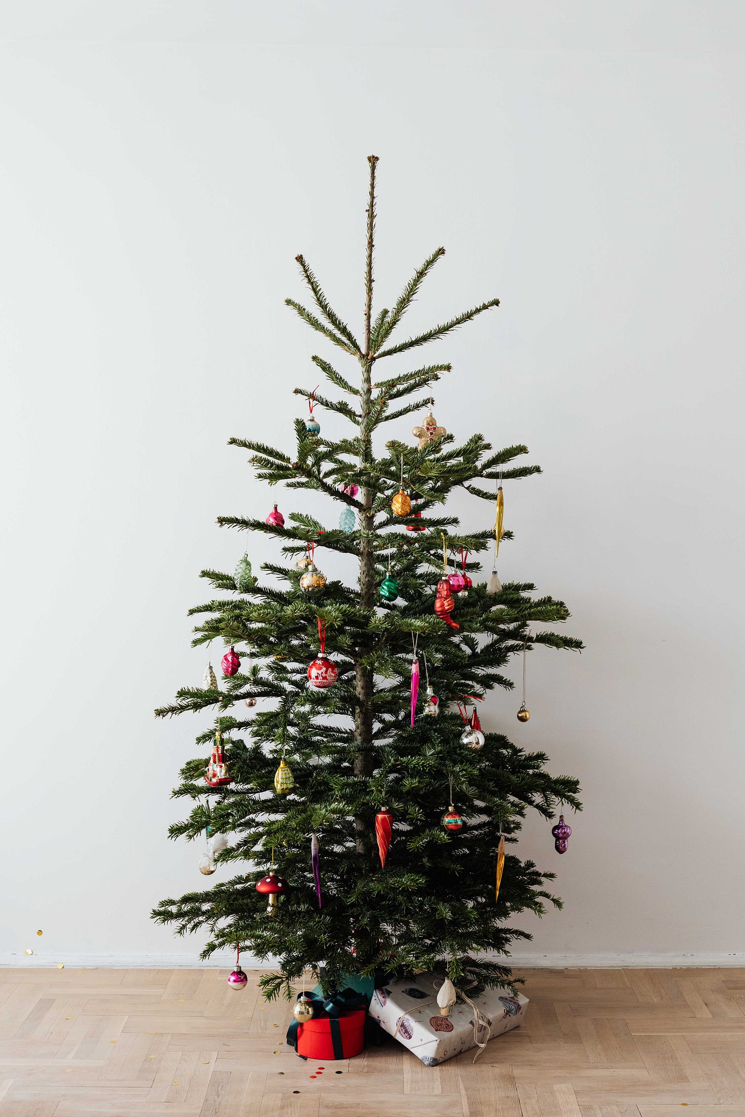 christmas tree, white background, colourful glass decorations in jewel tones and a few gifts under the tree wrapped in the same colourscheme.