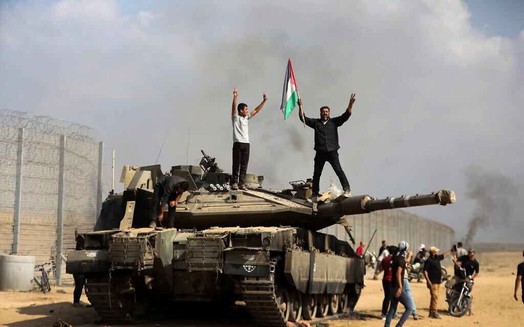 Gazans celebrate by a destroyed Israeli tank at the broken Israel-Gaza border fence, east of Khan Younis, October 7, 2023. (AP Photo/Yousef Masoud)