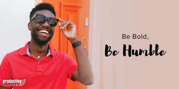 A man stands in front of an orange door, laughing and reaching for his sunglasses. Text Overlay: Be Bold, Be Humble. A man stands in front of an orange door, laughing and reaching for his sunglasses. Text Overlay: Be Bold, Be Humble.