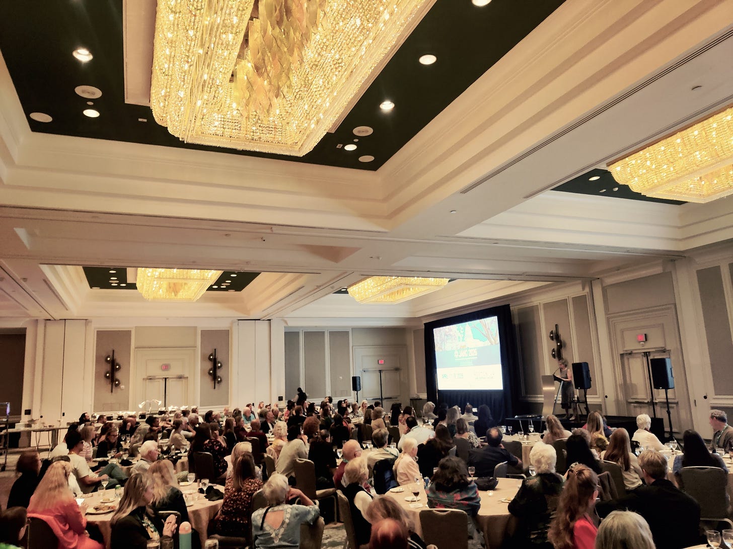 JAHC ballroom in Reston, Virginia, with crystal chandeliers, attendees at round tables, and a presenter at the lectern.