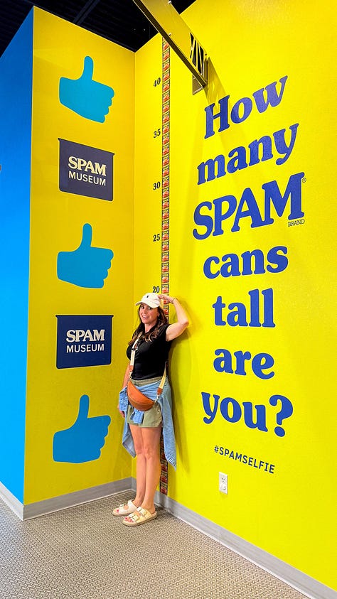 SPAM displays, a wall of colorful SPAM cans, and one person measuring their height against a SPAM can wall
