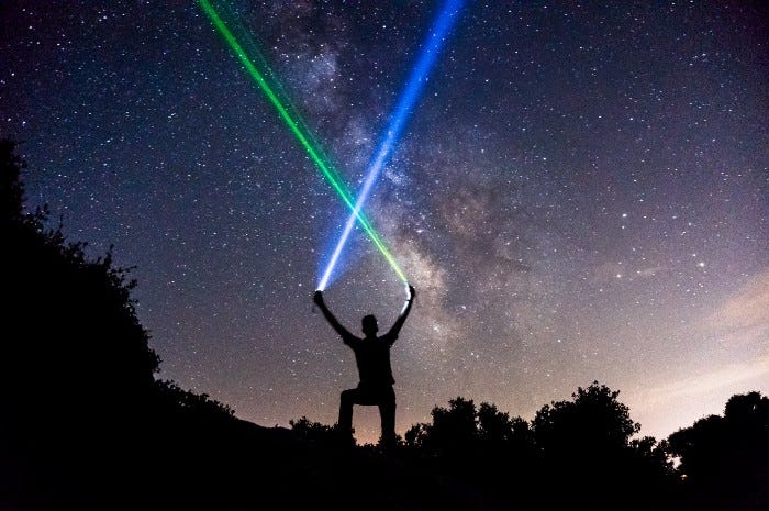A person holding green and blue flashlights at night with the background of a starry sky to try and raise attention. A person holding green and blue flashlights at night with the background of a starry sky to try and raise attention.