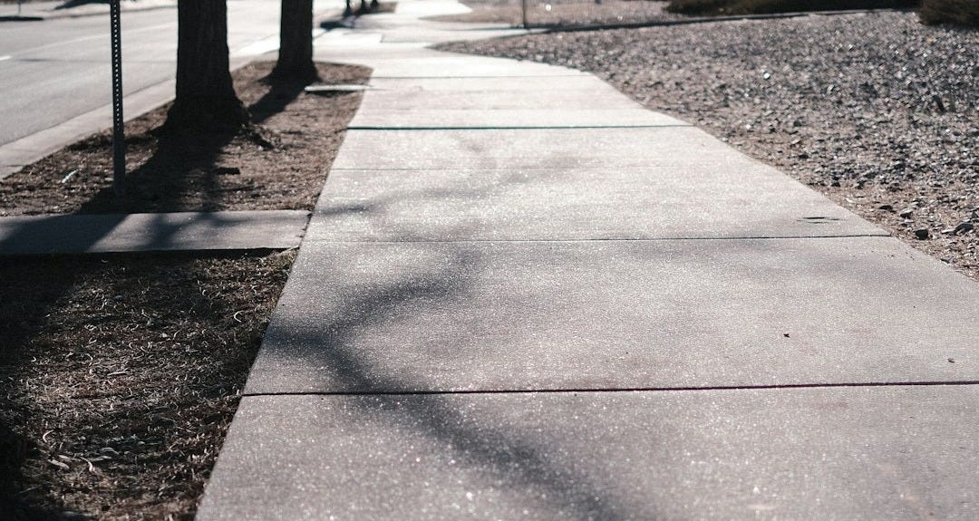 a sidewalk with a tree on the side of it a sidewalk with a tree on the side of it