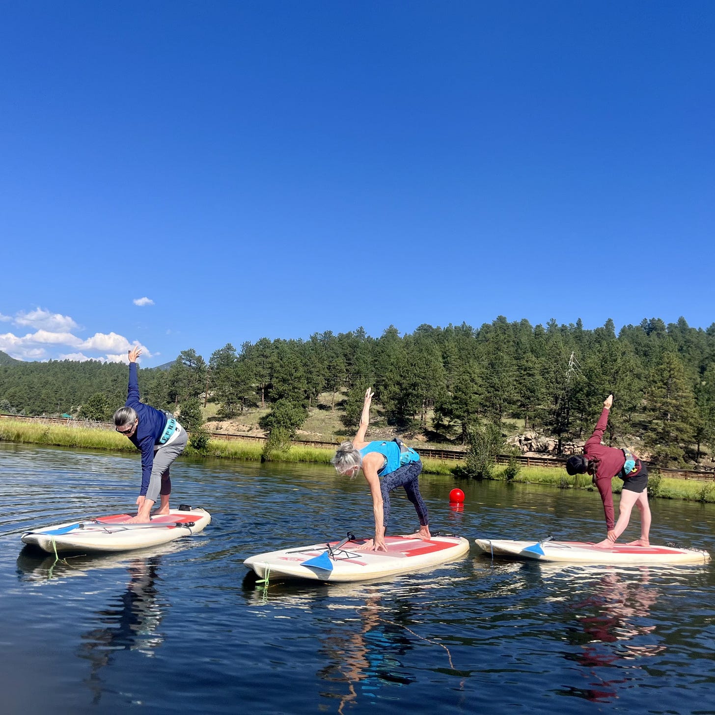 three women in revolved triangle pose on stand-up paddleboards on the lake three women in revolved triangle pose on stand-up paddleboards on the lake