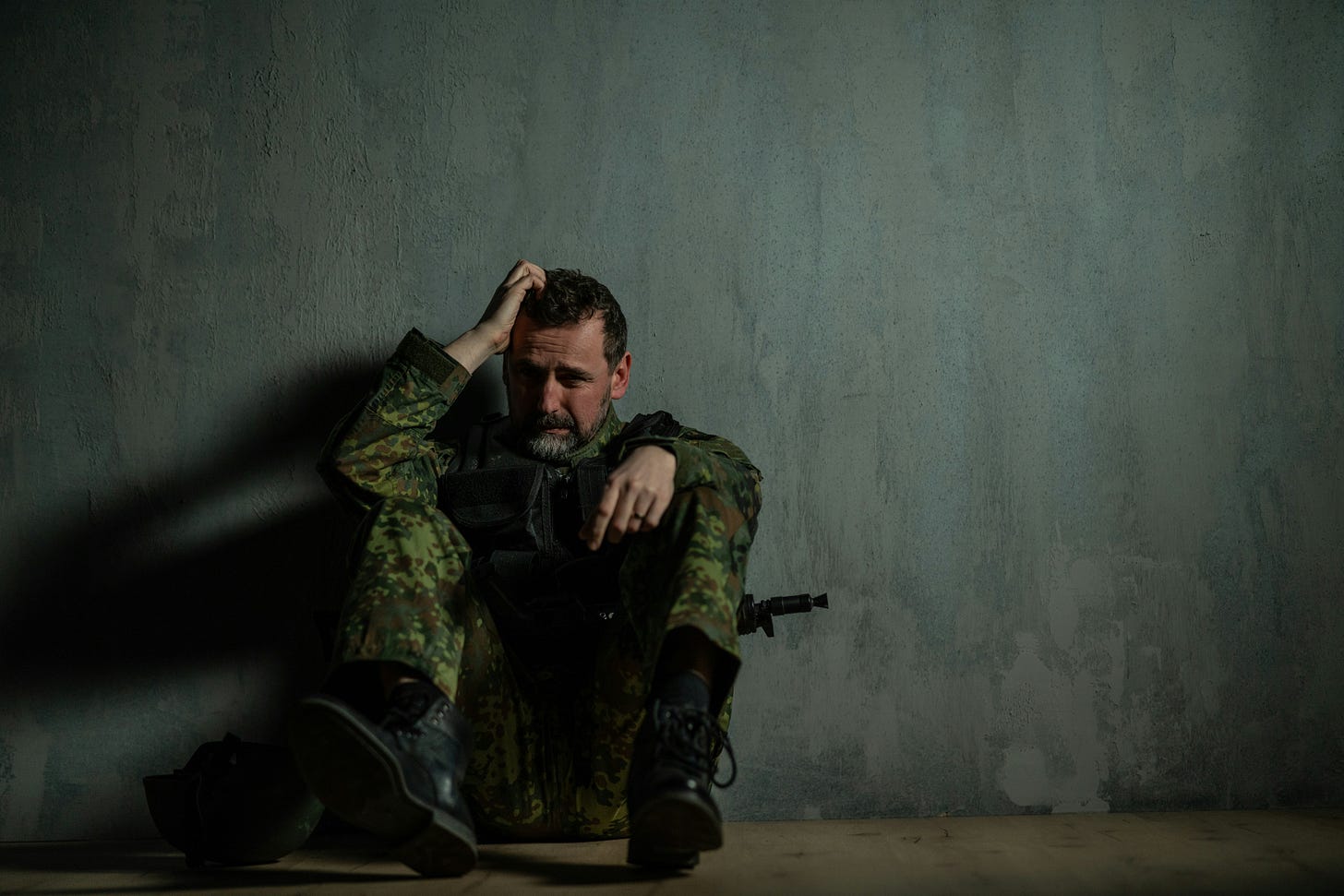 A crying soldier sits against a green wall. 