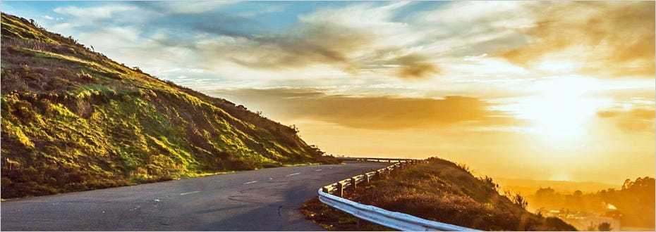 An empty mountain road glows from the sunlight of a rising sun.