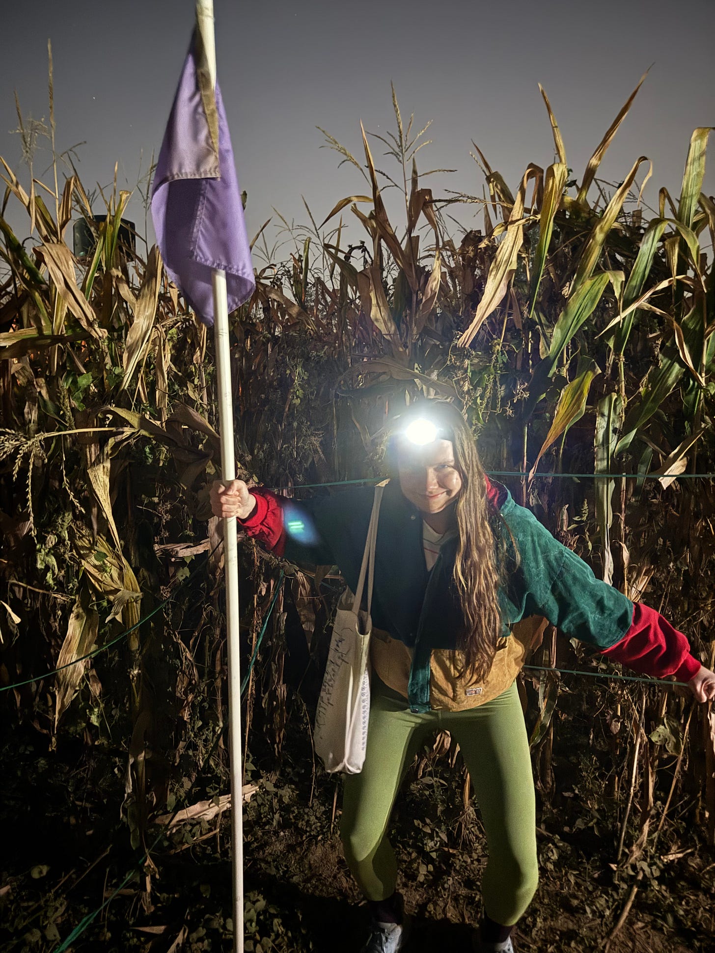 A photo of the author in a corn maze holding a purple flag