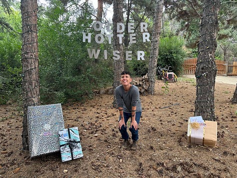 Image 1: Andrea Gibson opens a present under banner than reads "Older, Hotter, Wiser". Image 2: Many many meticulously wrapped birthday presents for Andrea. Image 3: Andrea Smiling under "Older Hotter Wiser" Birthday Banner