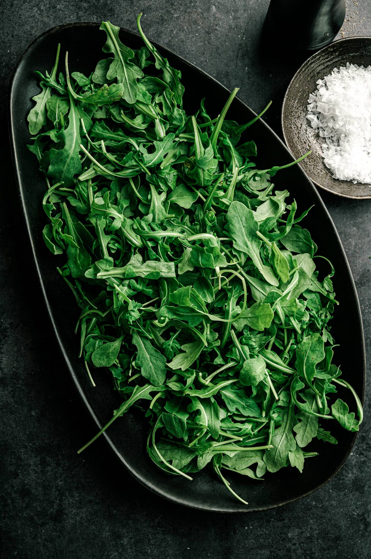 arugula salad rocket greens in a black bowl on. dark table. a