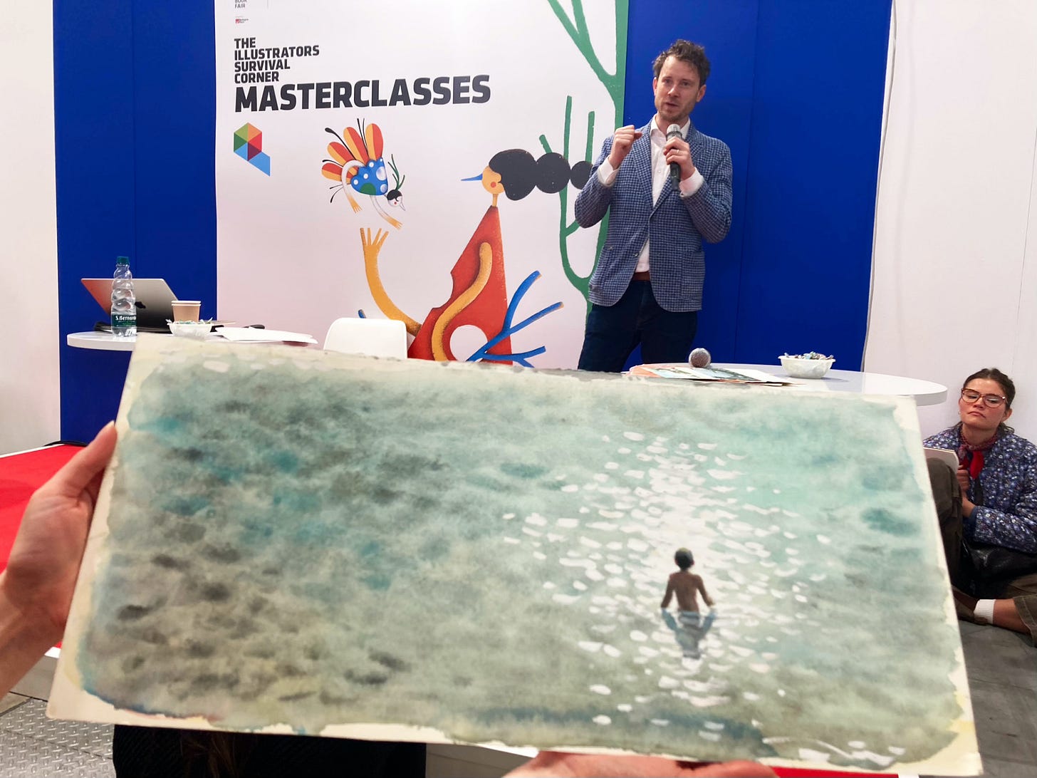 A photograph showing illustrator Sydney Smith and one of his paintings in a masterclass at the Bologna Childrens Book Fair 2025