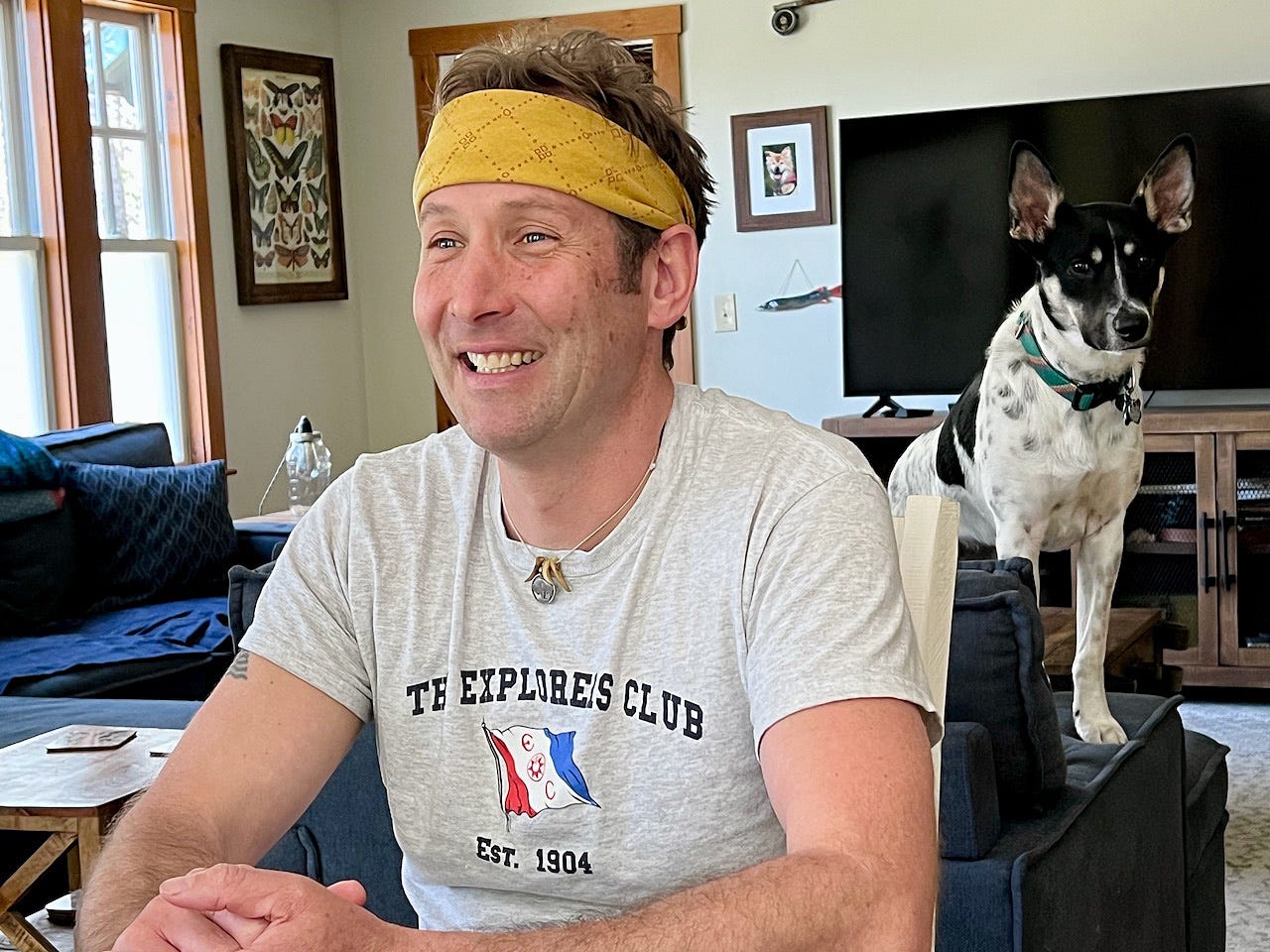 A person wearing a yellow headband and sitting in a living room with a dog

Description automatically generated