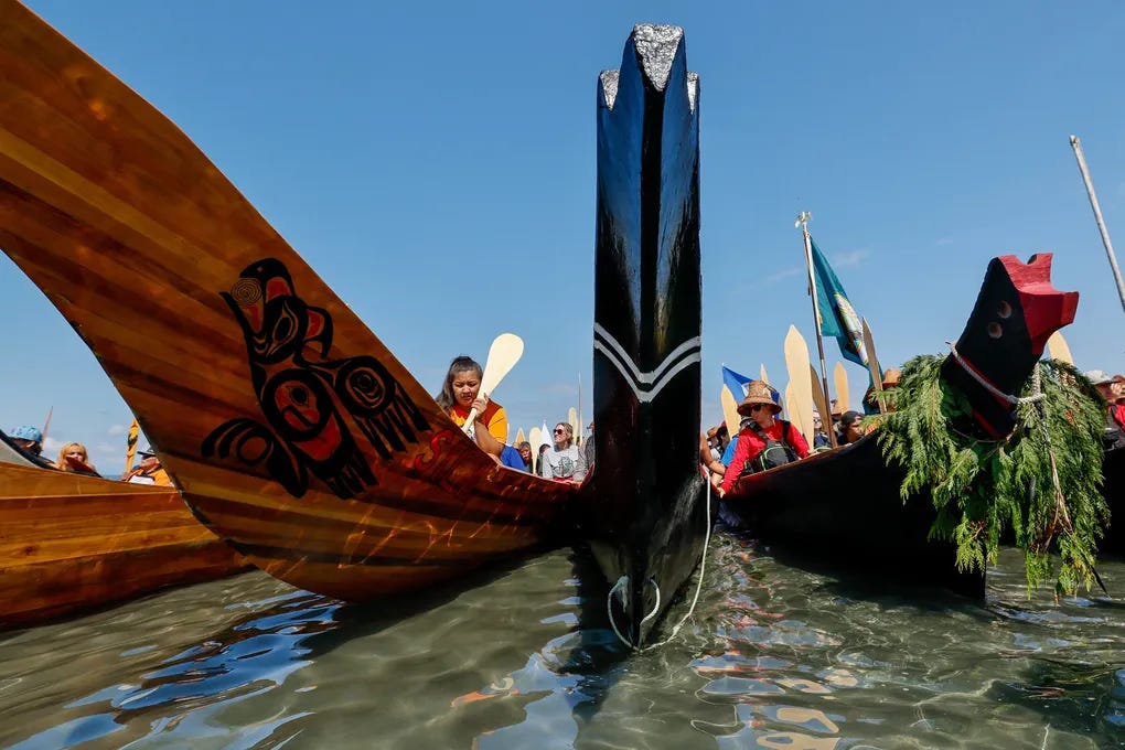 The sweeping bow of the Sila canoe reflects the ripples of the water just off of Alki Beach as the canoes wait to ask permission to come ashore on the final leg of the 2023 Canoe Journey. (Jennifer Buchanan / The Seattle Times)