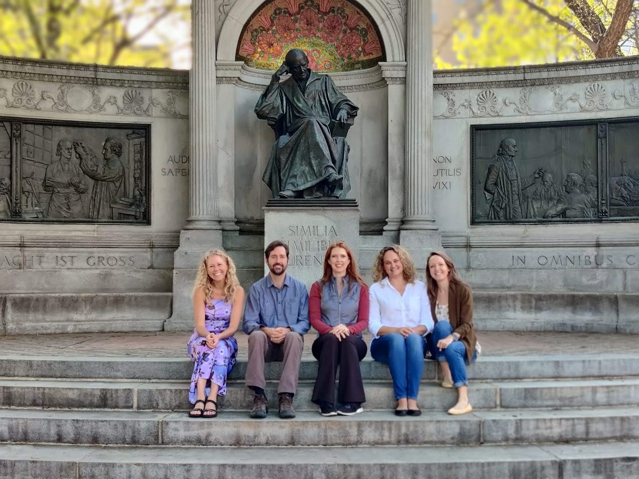 Five attendees seated on the steps of the Hahnemann Monument in Washington, D.C., honoring the founder of homeopathy. 