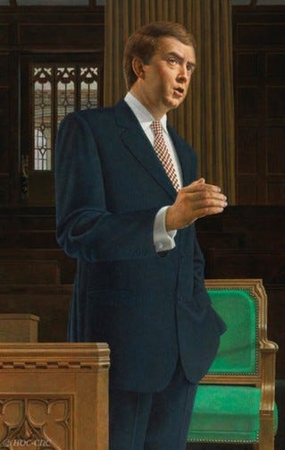 Joe Clark standing in a parliamentary chamber, facing slightly to the left as if speaking. He wears a dark blue suit, white shirt, and a patterned tie. His right hand is raised with fingers slightly apart in a speaking gesture, and his left hand rests near his pocket. Behind him is a green-upholstered chair and a wooden desk, with dark wood paneling and a tall, vertically striped curtain in the background. The lighting is even, highlighting his face and suit. Joe Clark standing in a parliamentary chamber, facing slightly to the left as if speaking. He wears a dark blue suit, white shirt, and a patterned tie. His right hand is raised with fingers slightly apart in a speaking gesture, and his left hand rests near his pocket. Behind him is a green-upholstered chair and a wooden desk, with dark wood paneling and a tall, vertically striped curtain in the background. The lighting is even, highlighting his face and suit.
