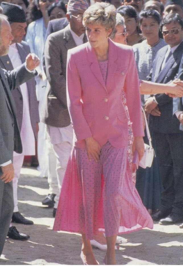 This may contain: an older woman in a pink suit and matching shoes is walking with other people behind her This may contain: an older woman in a pink suit and matching shoes is walking with other people behind her