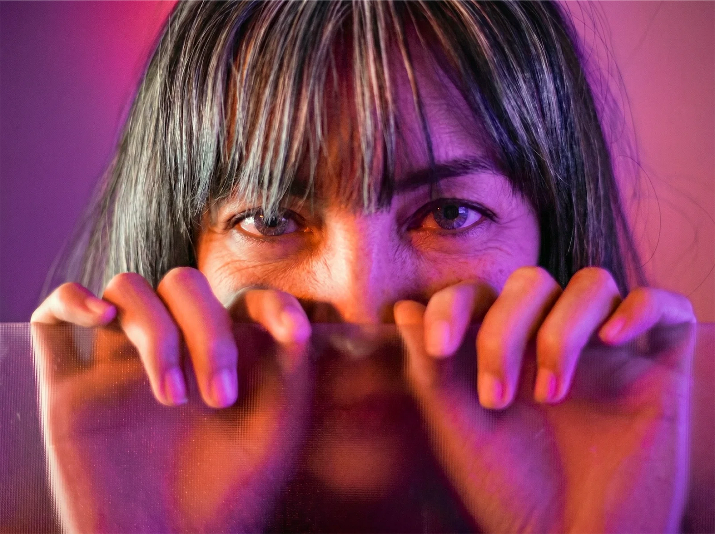 Woman holding onto a translucent panel under pink and purple light, reflecting on dealing with setbacks and failure when setting boundaries Woman holding onto a translucent panel under pink and purple light, reflecting on dealing with setbacks and failure when setting boundaries