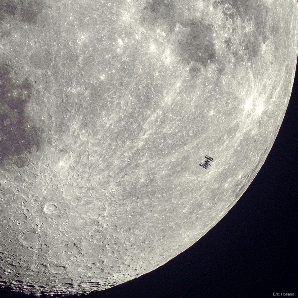A detailed view of part of Earth's Moon is shown with
many craters visible. On the lower right, silhouetted against
the comparatively bright Moon, is a small dark silhouette of
the International Space Station. Many of the solar panels on
the station are discernable. 
Please see the explanation for more detailed information.